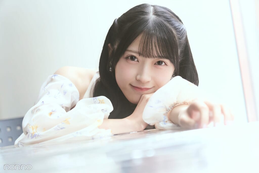 机にもたれかかり、こちらを向いて少し微笑むAKB48 佐藤綺星さん