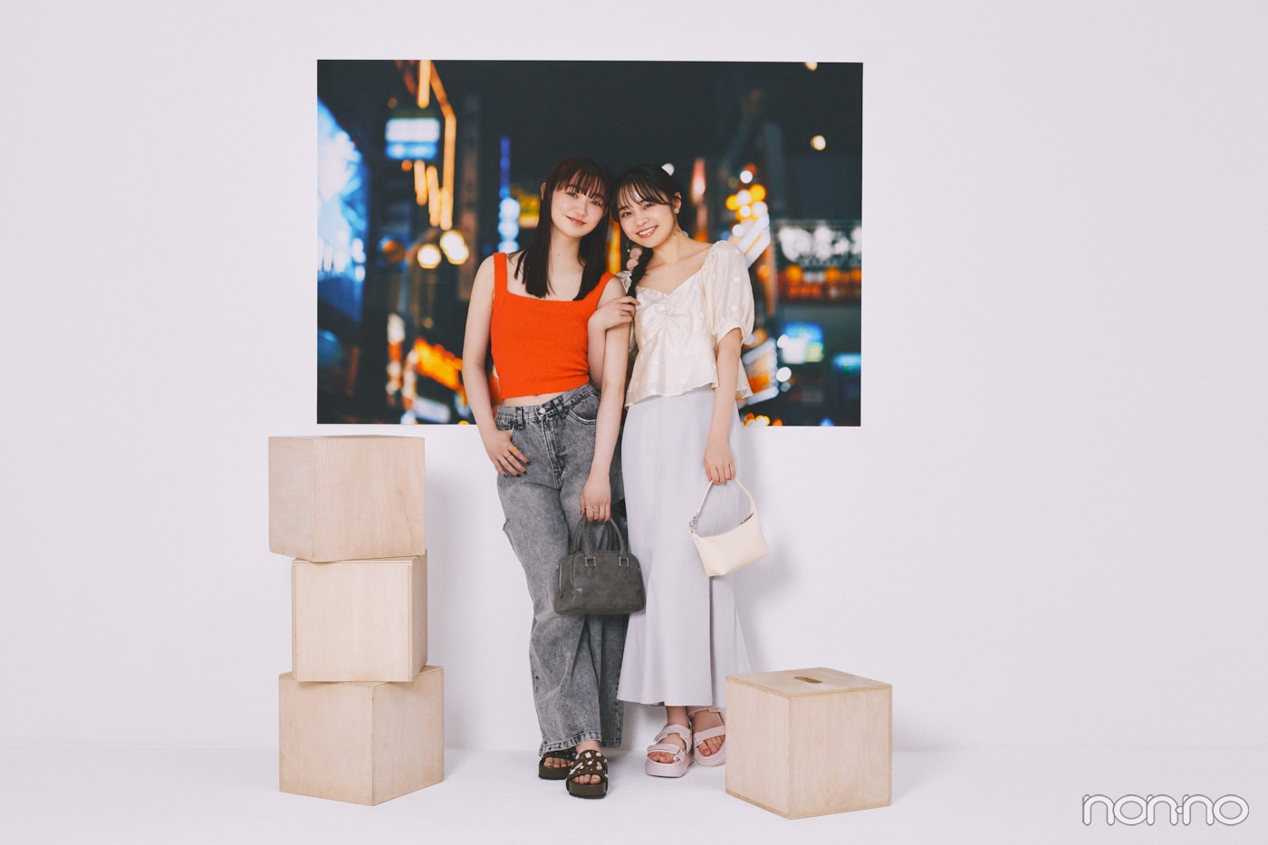 夜の飲食街の写真の前に立つ林芽亜里と小宮山莉渚