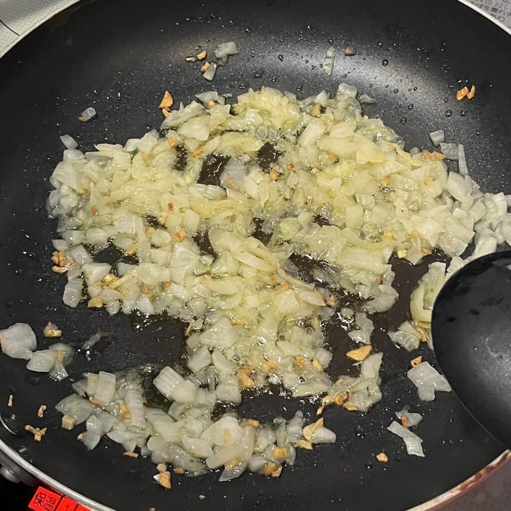 オリーブオイルをひいたフライパンで、ニンニクと玉ねぎを炒めている