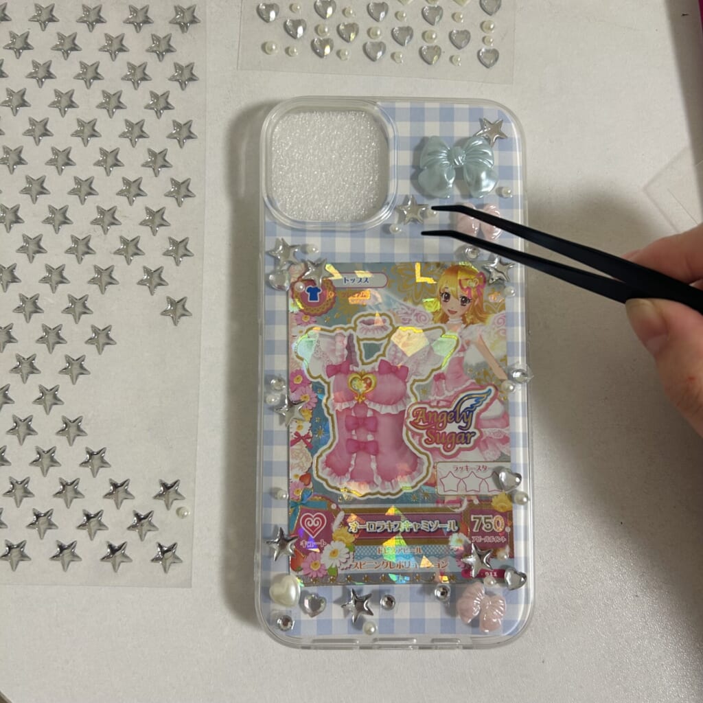 シールをピンセットでスマホケースに貼っている写真。