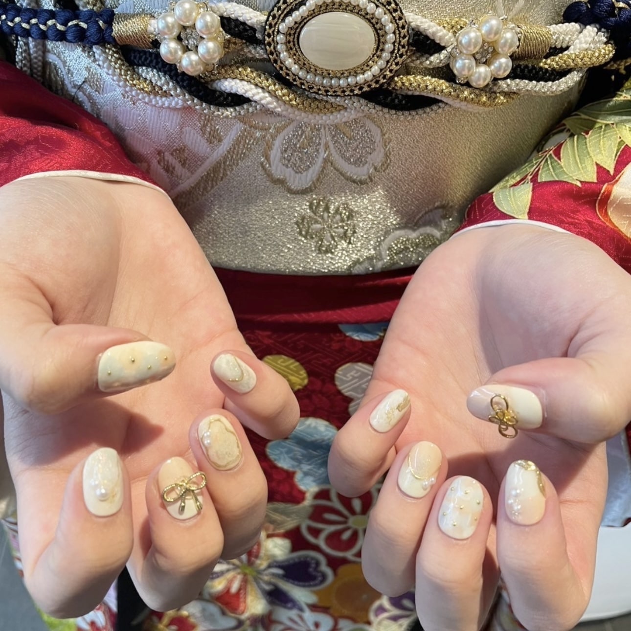 振袖を着た成人式ネイルの手元　白ベースでゴールドのリボンと水引パーツをつけたネイルデザイン