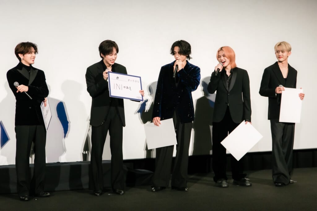 INIドキュメンタリー映画完成披露試写会でフリップを見せ談笑するメンバー