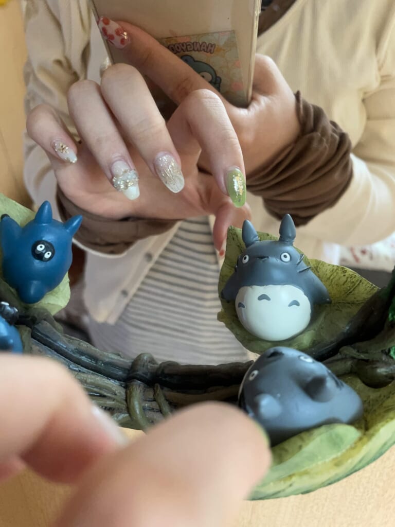 フレームにトトロがついた鏡越しにネイルを見せている