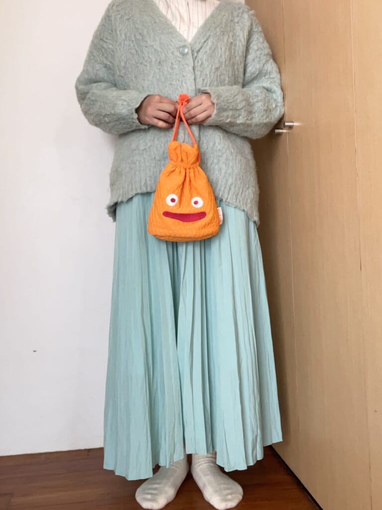 緑色のカーディガン、スカートにストライプのシャツ。カルシファーのポーチを持っている