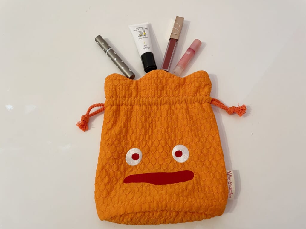 カルシファーの巾着を口を開いている、上にコスメを並べている