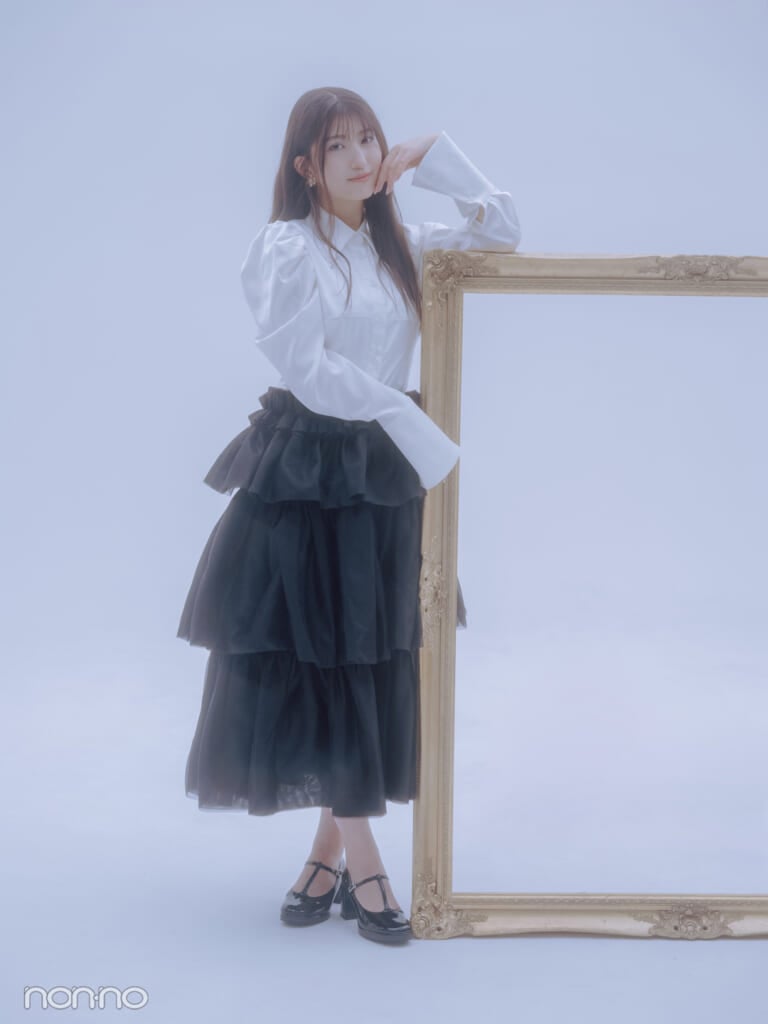白いシャツと黒いティアードスカートを着て、大きな額縁にもたれるモーニング娘。’25羽賀朱音さんの全身カット