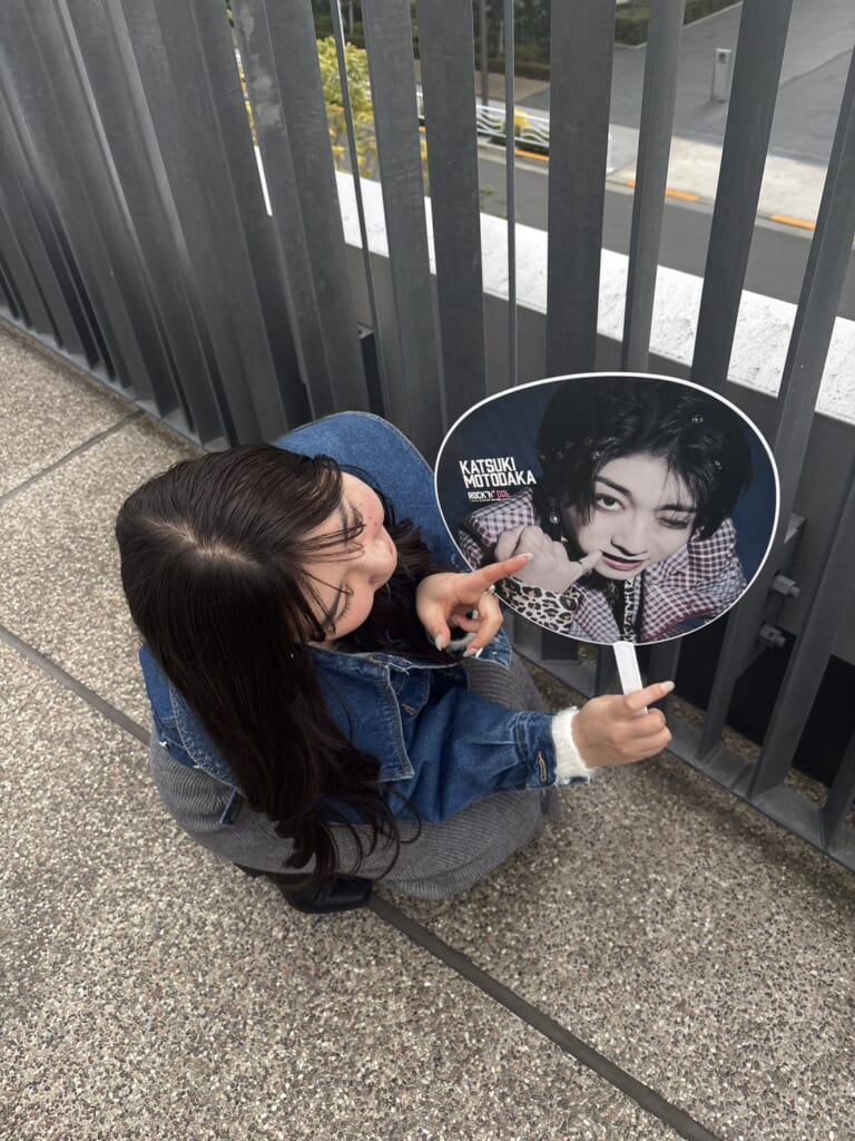 推しのうちわを持って、指差ししてしゃがんでいる写真