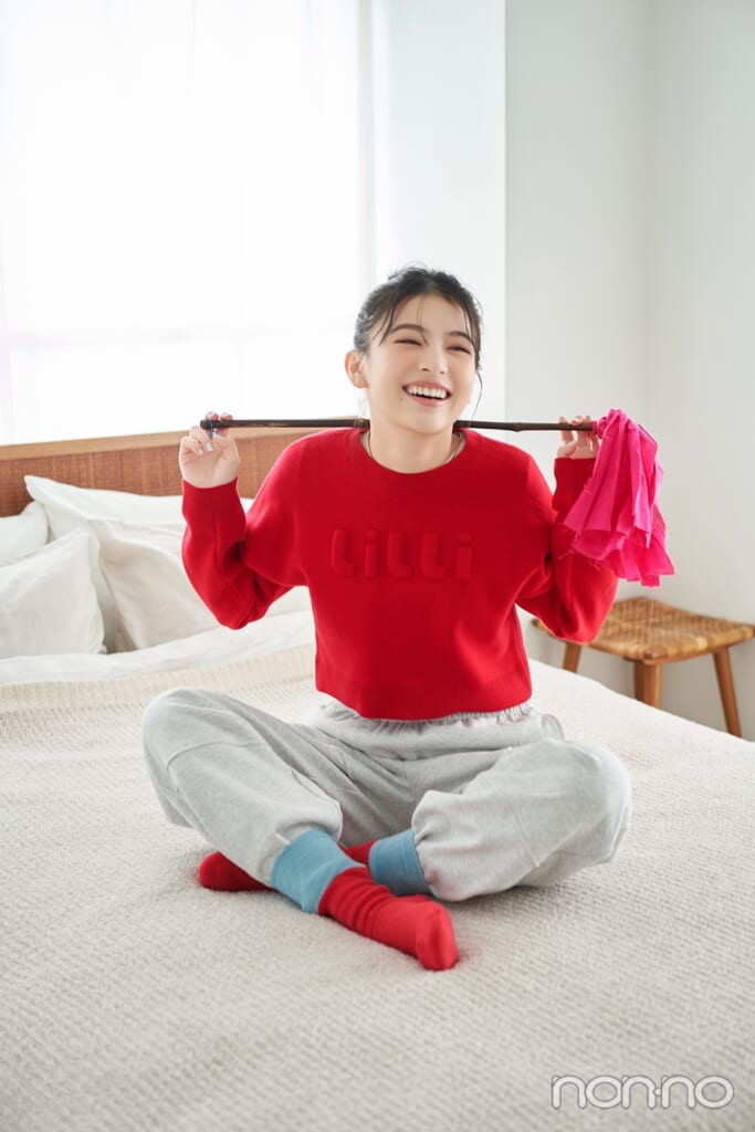 赤いニットにグレーのスエットパンツを履いてはたきを持つ出口夏希