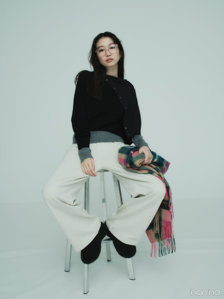 ユニクロのメリノクルーネックセーターをレイヤードで着こなし、カジュアルなパンツに合わせ、ハイチェアに座っている岡本夏美