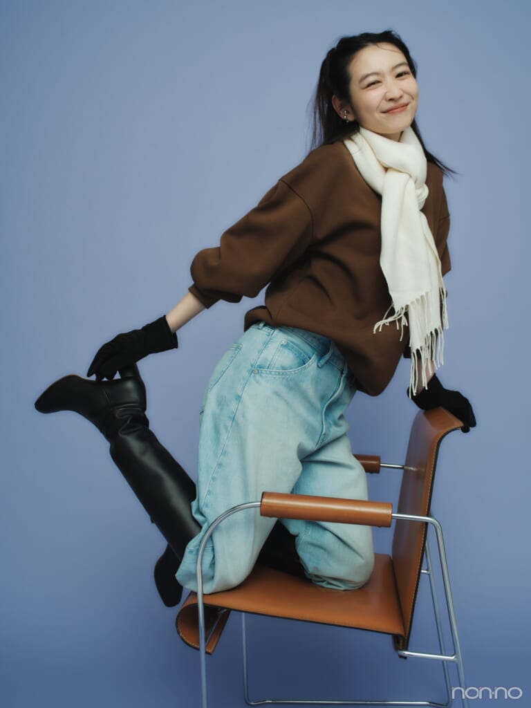 椅子に膝立ちになり、ユニクロ：シーのブラウンスウエットをデニム＆ブーツでカジュアルに着こなした岡本夏美