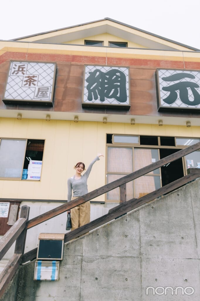 店前の階段で手を挙げる紺野彩夏