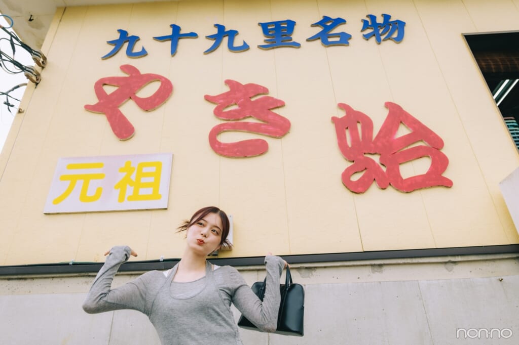 「やき蛤」の文字の前で手をひろげる紺野彩夏