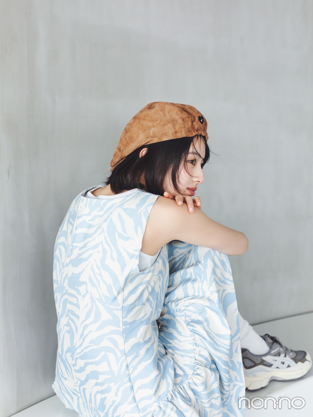 キャメルの帽子にゼブラ柄のワンピースを着て横向きに座る出口夏希