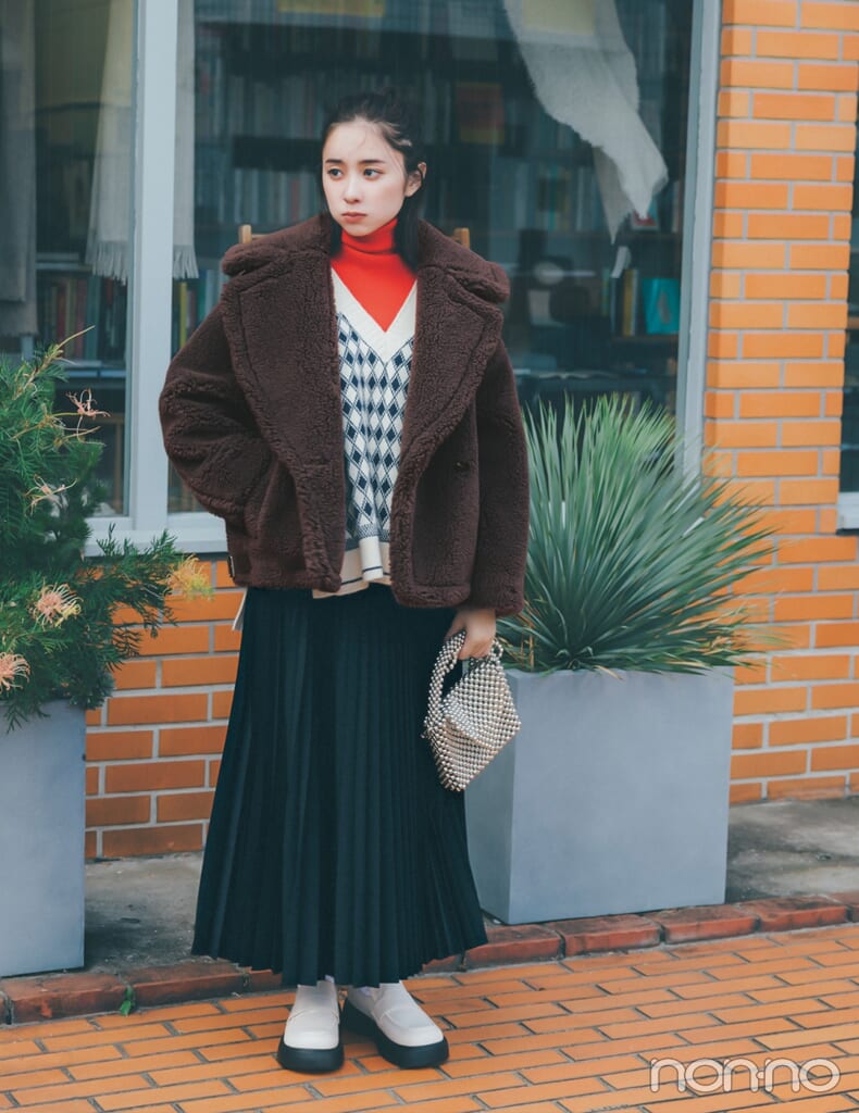 赤タートルニットとベストとプリーツスカートを合わせた赤ニットコーデの女性