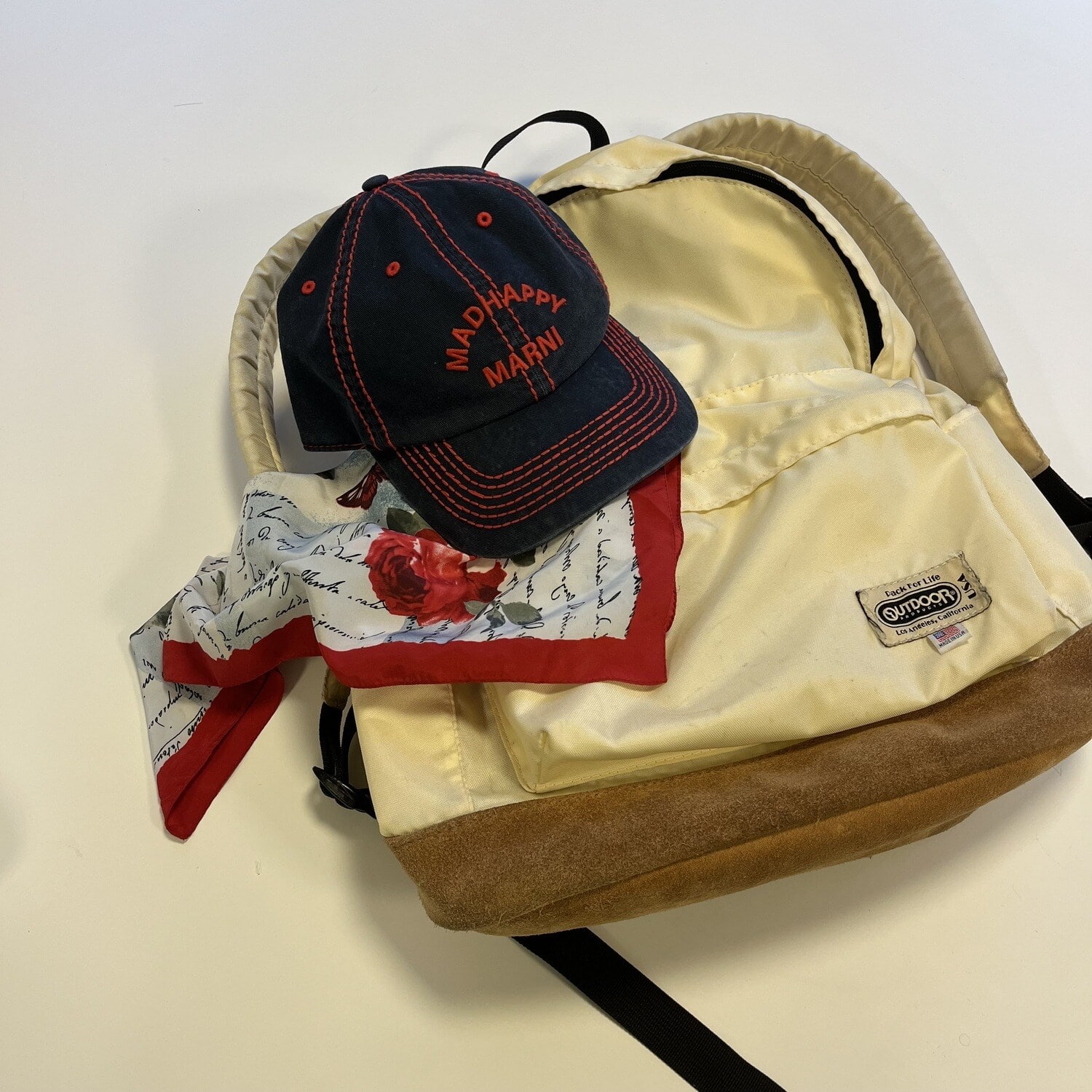 机に置かれたOUTDOOR PRODUCTSの白いデイパックとMARNIのキャップ