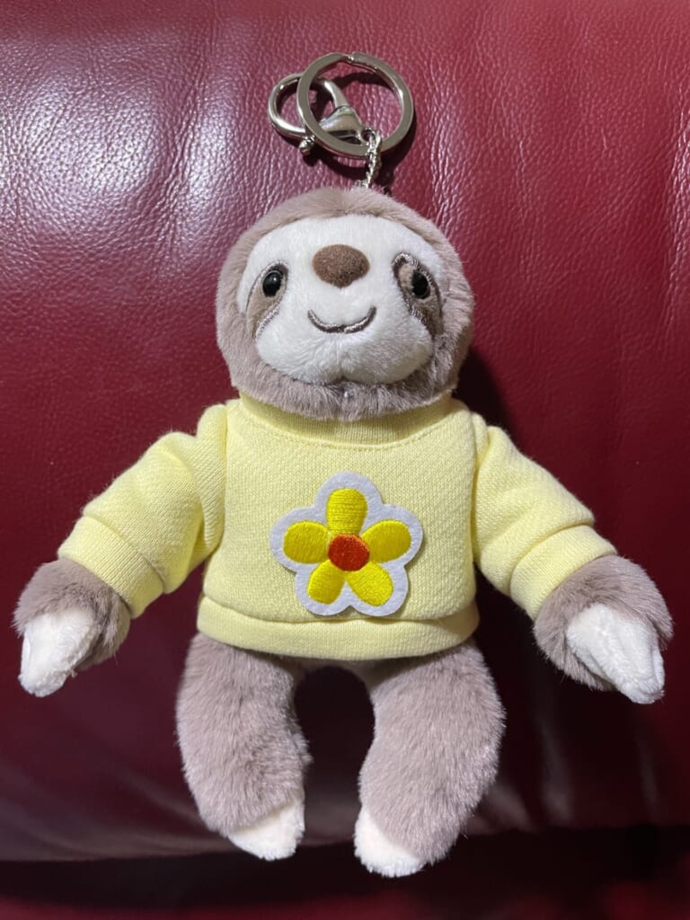 なまけもののキーホルダー。花が付いた黄色い服を着ている。