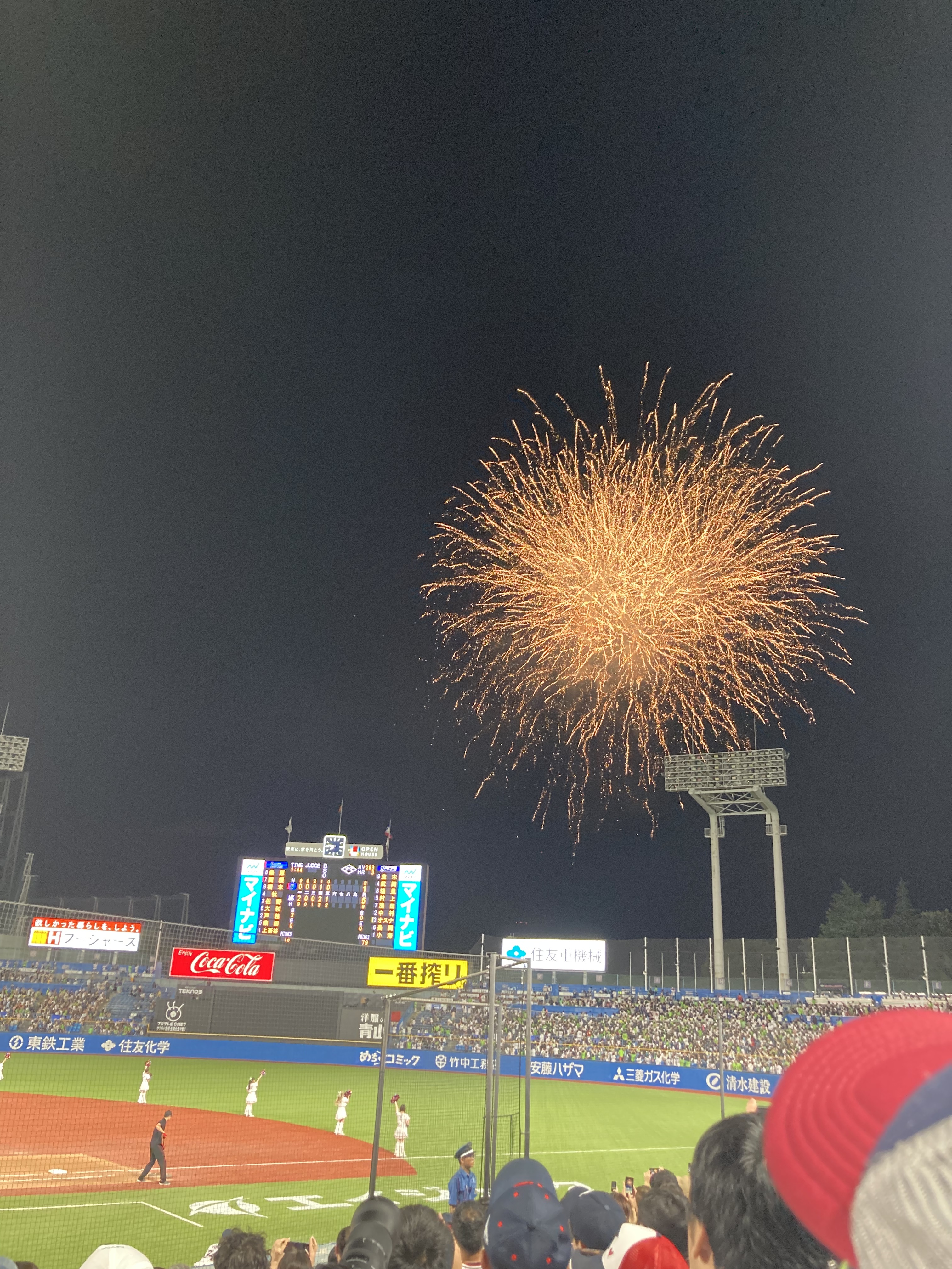 試合の回の間に打ち上げられた花火。オレンジのような花火が広がっている。電光掲示板と写っている写真。