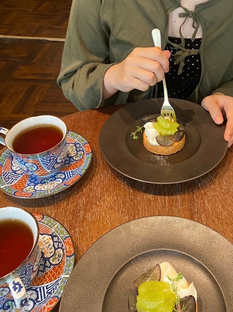 「TINA:JOJUN」のキラキラしたベロア素材のトップスとリボン付きカーディガンを着た女の子が、蔵前のカフェ「from afar」の葡萄のタルトを食べている写真