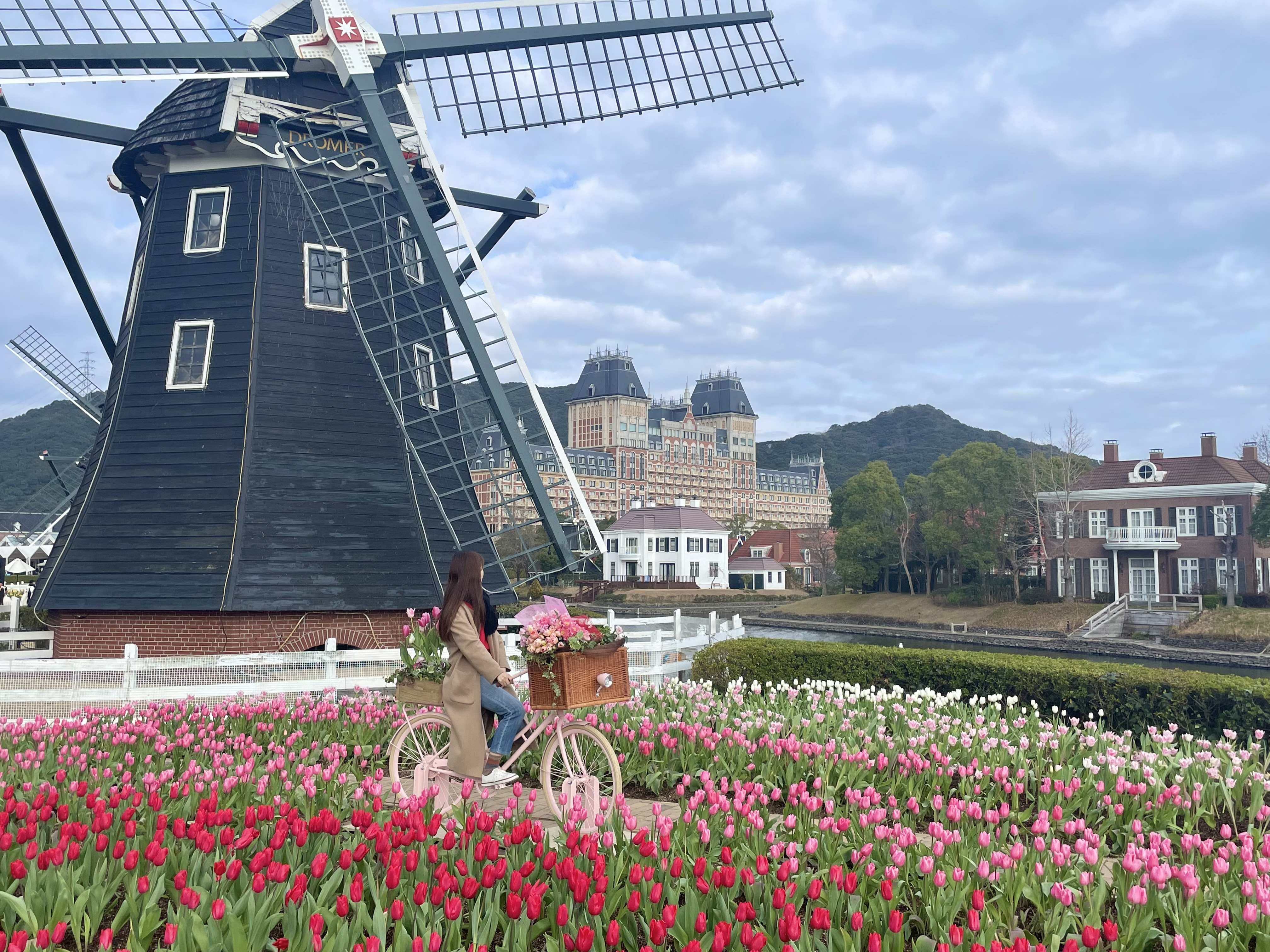 ハウステンボス フラワーロード チューリップ畑の中で自転車に乗っている様子 背景に風車