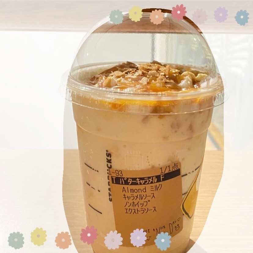 スタバのホリデーシーズン第2弾。期間限定で登場している、スターバックス新作「バターキャラメル ミルフィーユ フラペチーノ」の写真です。白い背景と茶色い机の上に、フラペチーノが置かれています。フラペチーノは、薄い茶色で、背面にシールが貼ってあります。茶色のシールには、黒い文字で「T バターキャラメルF、Almondミルク、キャラメルソース、ノンホイップ、エクストラソース」と私おすすめのカスタマイズが印字されています。