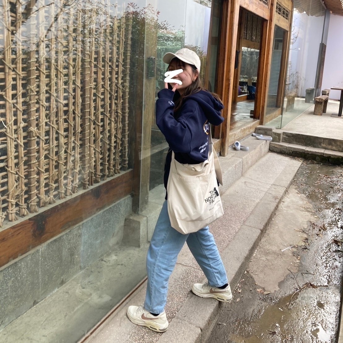 水色のデニムに紺色のロゴパーカーを着て、帽子をかぶった写真。